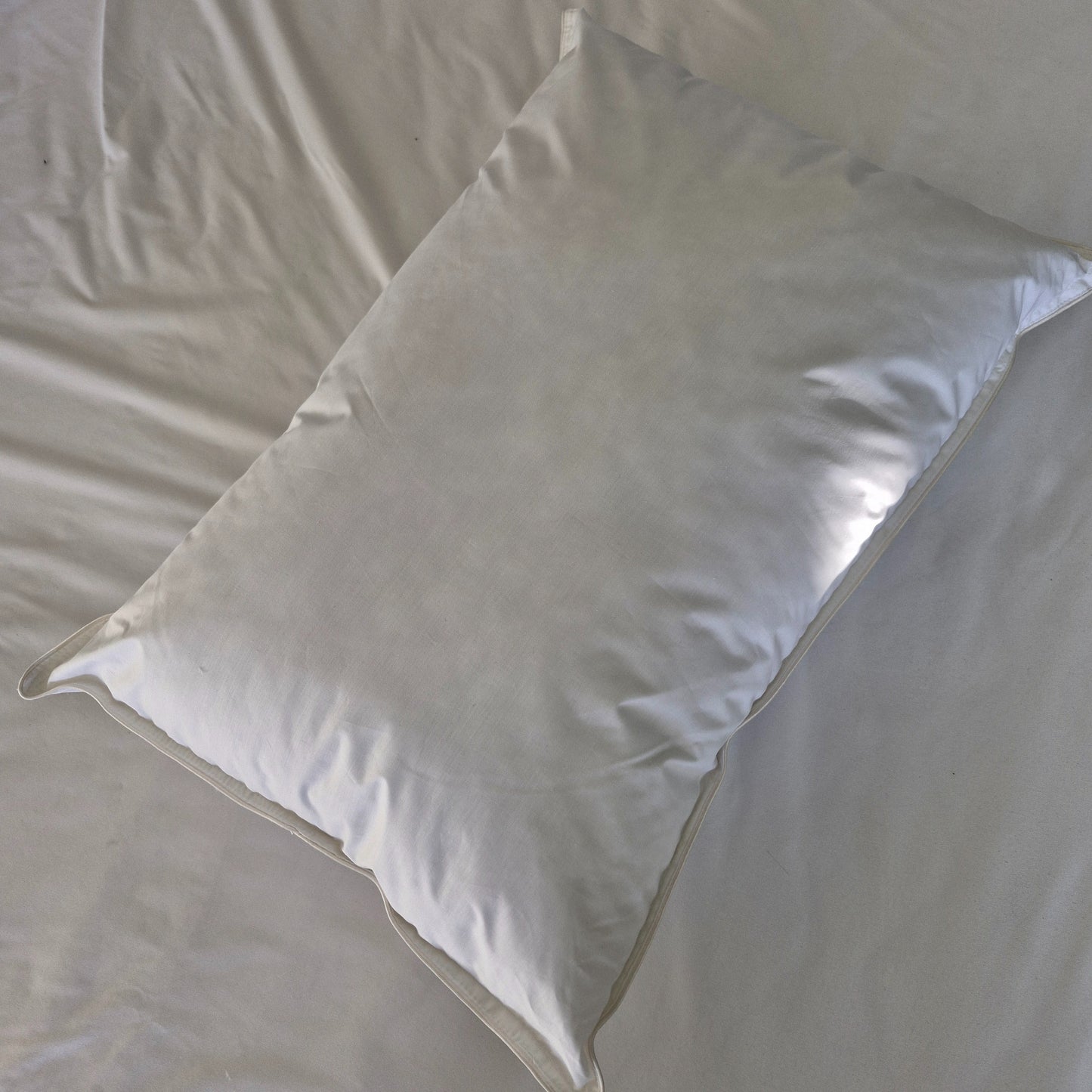 White waterproof cotton pillow laying on a white bed sheet