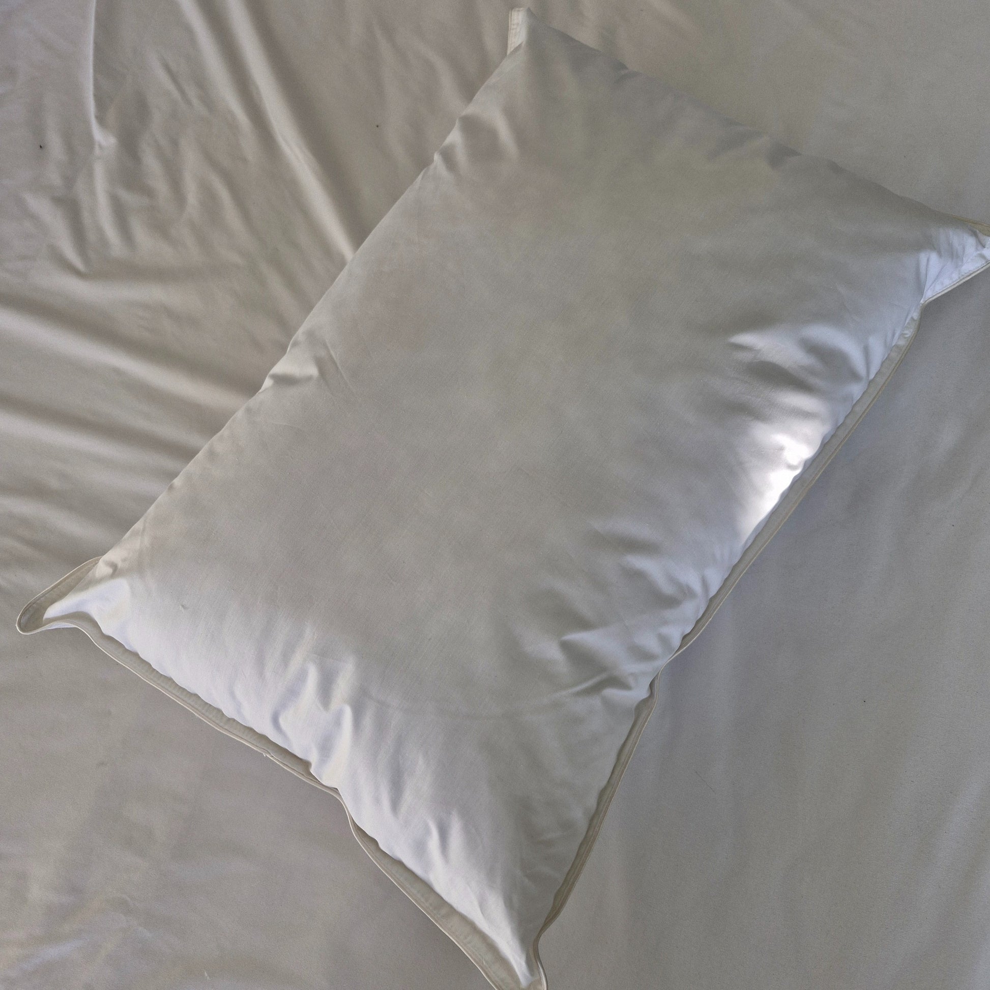 White waterproof cotton pillow laying on a white bed sheet