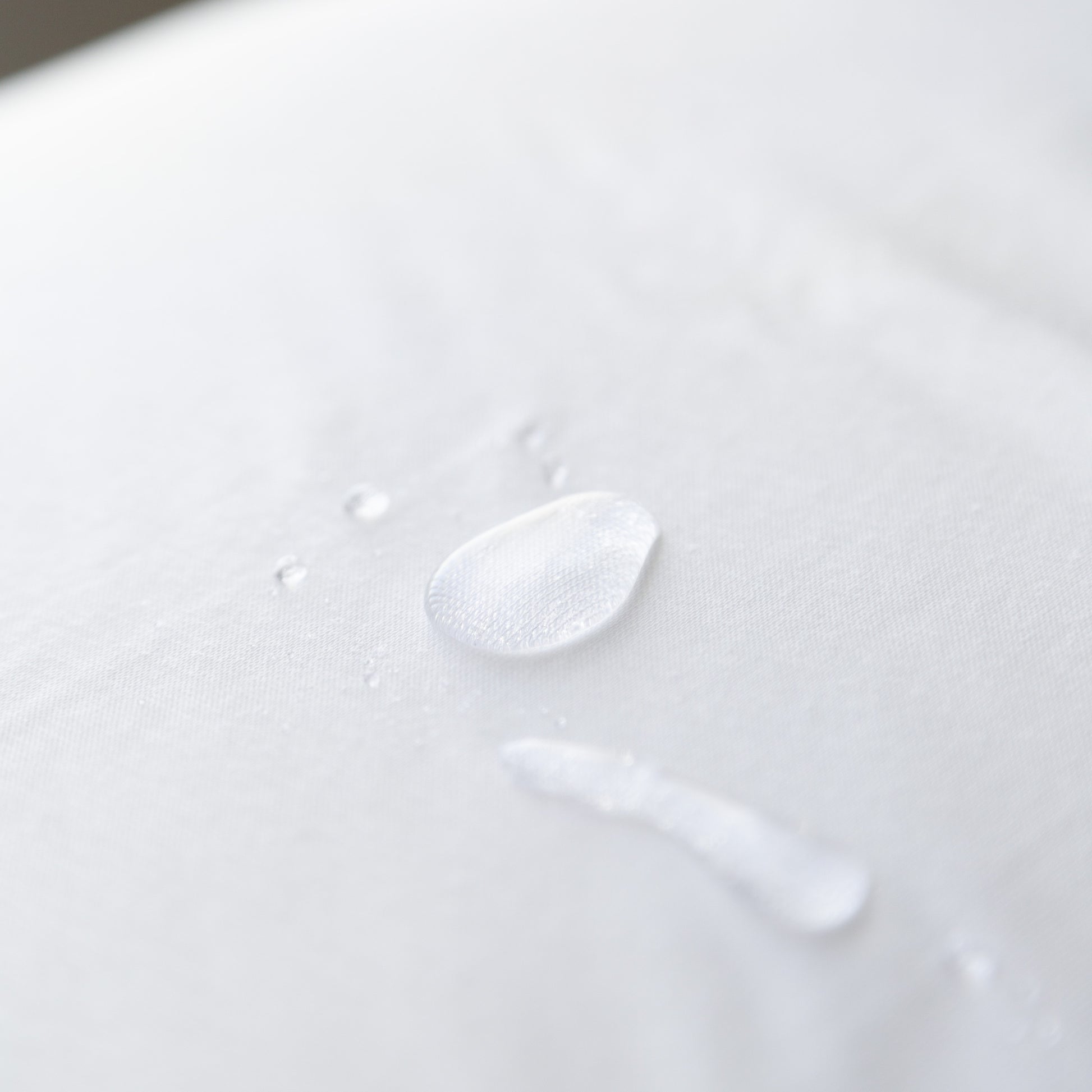 Close-up of a water droplet on a white cotton waterproof pillow